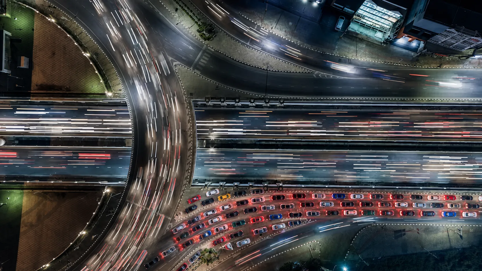 Aerial view of sports cars gridlocked on one interchange while traffic streaks past around them.